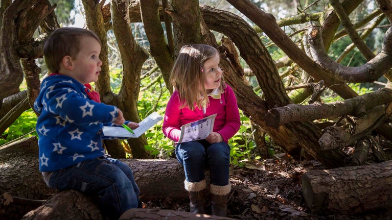Two children in jumpers sitting in a tree den at Tyntesfield